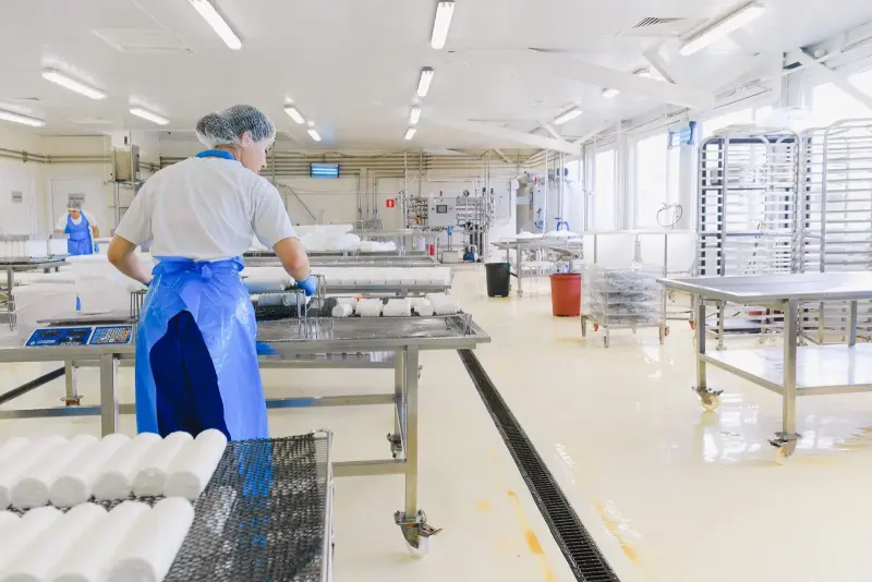 Colaboradora com touca e avental em linha de produção de alimentos.