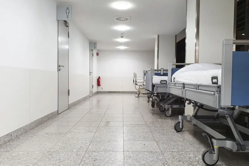 Corredor hospitalar limpo, com leitos alinhados junto à parede.