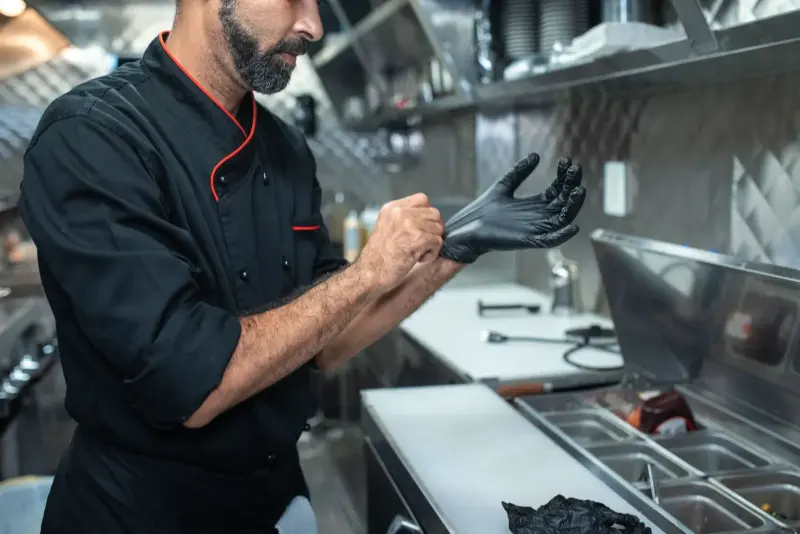 Chef calçando luvas descartáveis em cozinha profissional de inox.